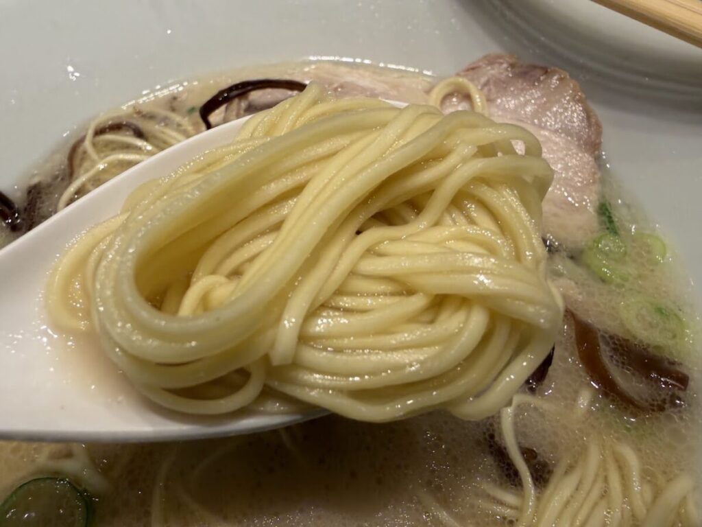 麺をレンゲの上に乗せてスープと絡ませている一風堂の定番メニュー白丸元味の写真